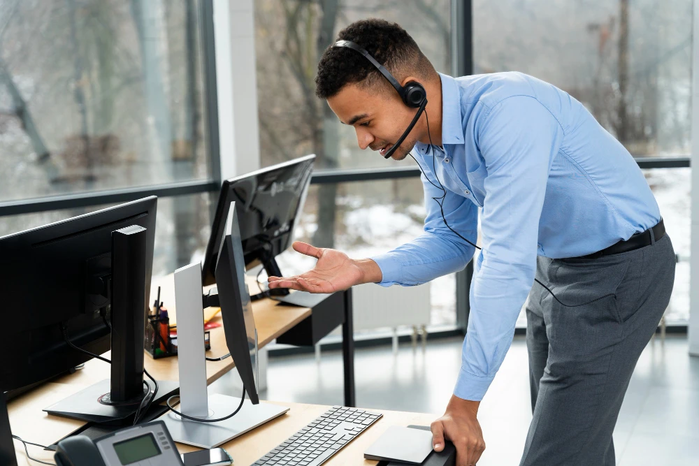 Technical support specialist wearing a headset assisting a client at a computer workstation.